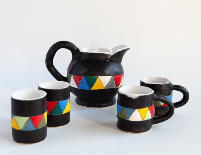 Black pitcher with coloured pattern and matching mugs.