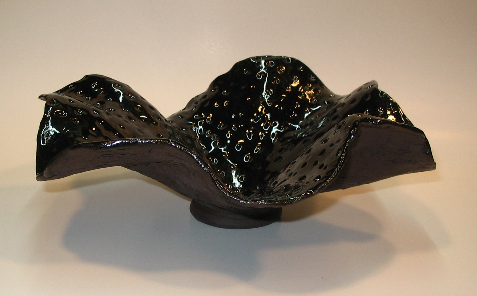 Black wavy bowl in black clay with glossy interior glaze and unglazed underside.