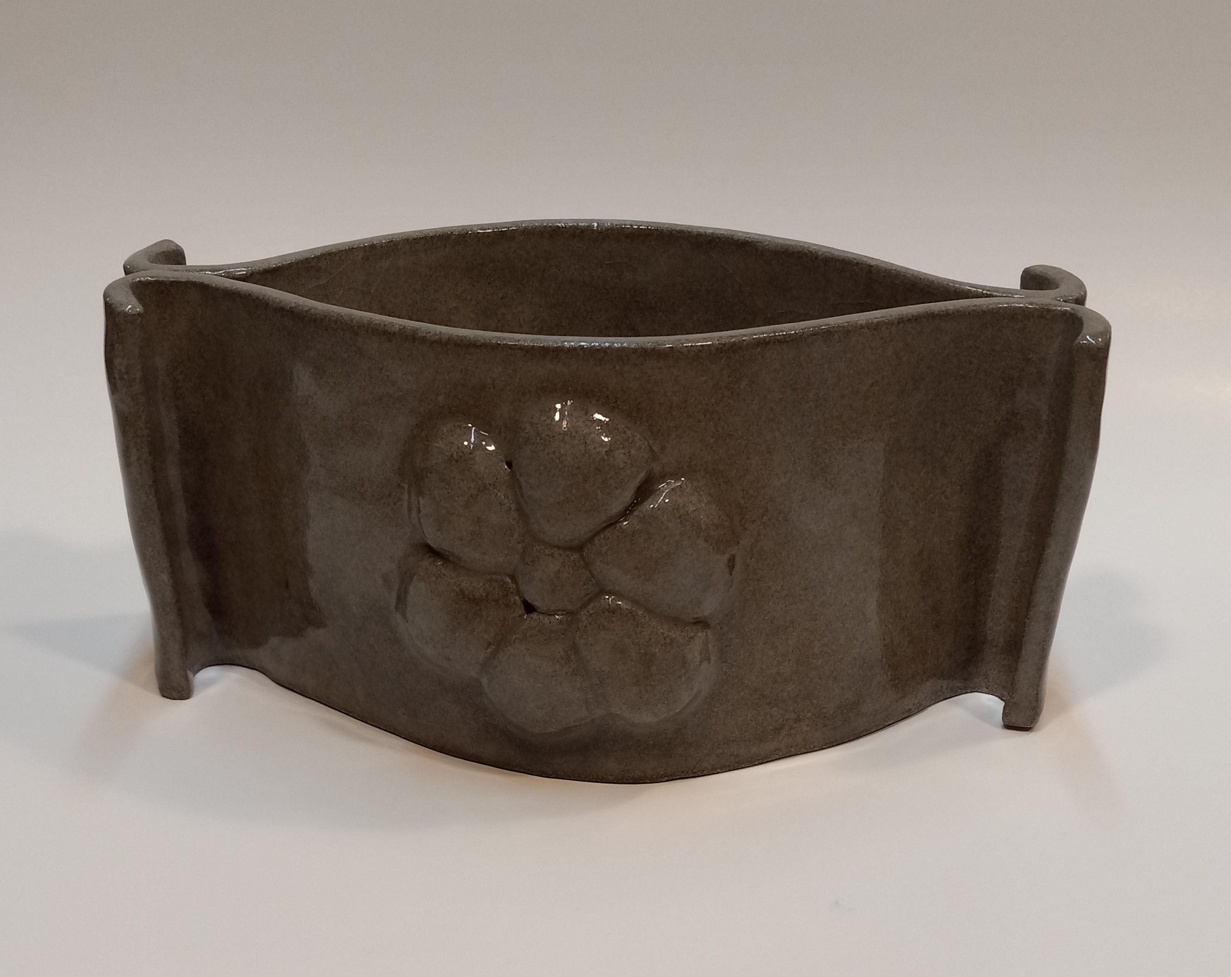 Bowl in dark granite with raised flower design, clear glazed. Can be decorative or used as container.